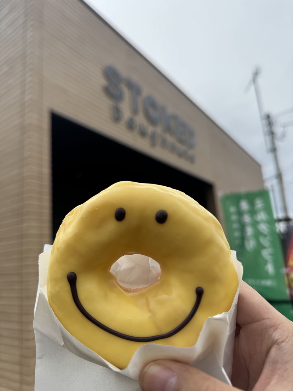 日本旅行中、店の前でCooperが手に持った黄色いスマイルドーナツ